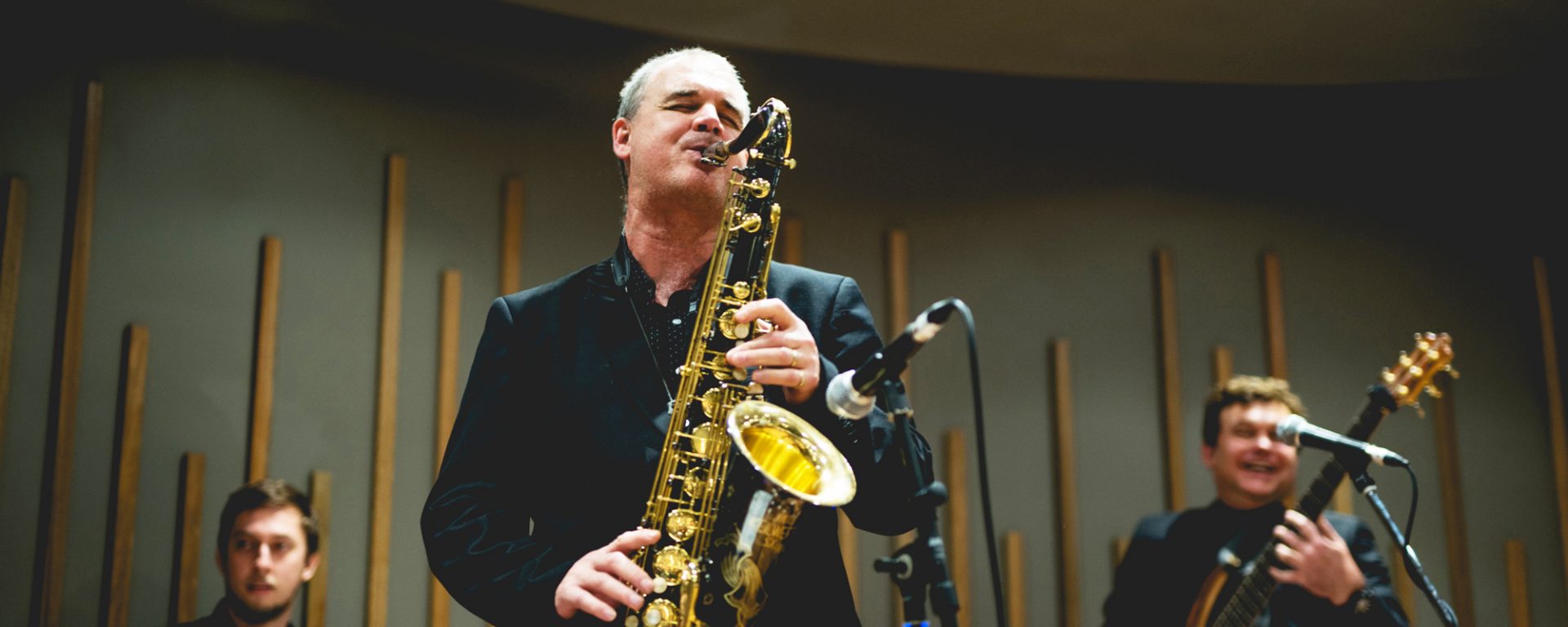 Andy Firth playing tenor saxophone live on stage with band in foreground